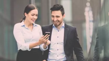 Zwei Personen gehen und lachen, während sie auf ein Handy schauen.